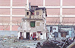 Ruine eines alten Hauses mit Bewohnern und herumliegendem Unrat vor einer hohen Betonwand
