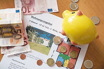 Ein gelbes Sparschwein zwischen Wohnungsangeboten und Geldscheinen und -münzen