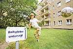 Ballspielendes Kind auf dem Rasen einer Wohnanlage