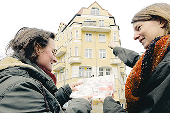 Personen mit Wohnungsanzeigen in der Hand vor einem Wohnhaus