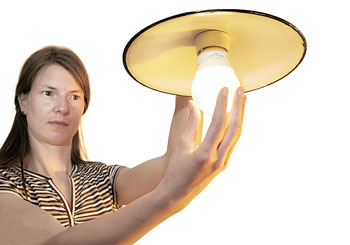 Eine Frau dreht eine Energiesparlampe in eine Leuchte