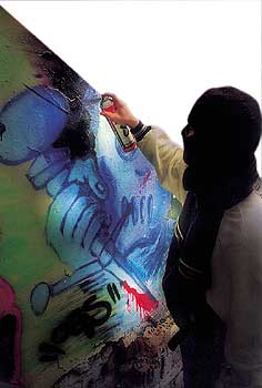 Vermummter Graffiti-Sprayer beim Besprühen einer Wand