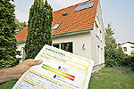 Hand mit einen Geb&auml;ude-Energieausweis vor einem Einfamilienhaus im Hintergrund