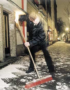 Mann, der vor einem Haus Schnee fegt