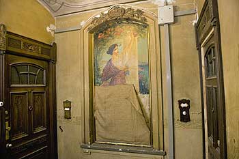 Wandgemälde in einem restaurierten Altbau-Treppenhaus: eine junge Frau mit leichtem Kleid streckt ihre Hand aus nach einem Rosenstrauch