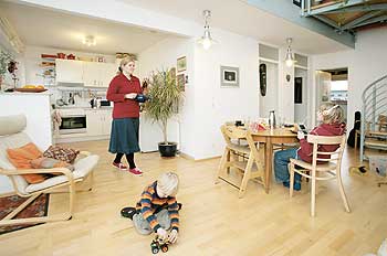 Großer Gemeinschaftsraum: die Mutter kommt aus der an den Wohnraum angrenzenden Küche, dort spielt der Sohn auf dem Fußboden