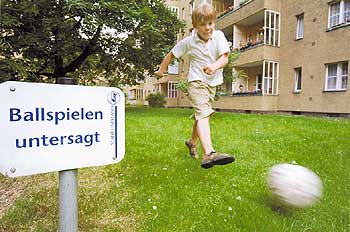 Ein Junge schießt einen Fußball. Daneben ein Schild mit der Aufschrift 'Ballspielen untersagt'
