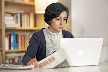 Frau mit Laptop und Immobilienteil der Zeitung