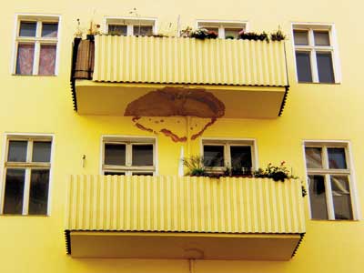 Gelbes Haus mit großem braunen Wasserfleck unter einem Balkon