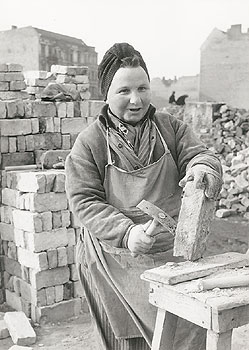 Trümmerfrau zwischen Häuserruinen beim Abklopfen von Steinen