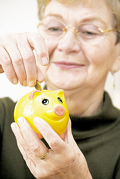 Seniorin steckt eine Münze in ein Sparschwein