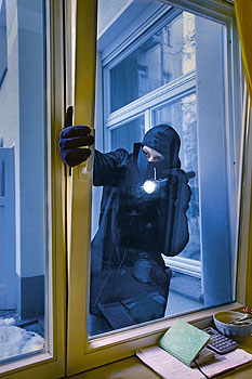 Ein Einbrecher greift durch ein angekipptes Parterre-Fenster