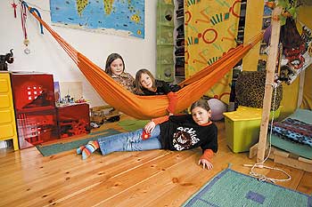 Kinder in einer Hängematte und auf dem Boden eines Kinderzimmers