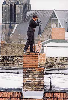 Schornsteinfeger beim Kaminkehren auf dem Dach eines Hauses