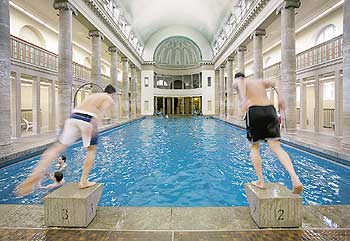 Historisches Berliner Hallenbad mit zwei von Startblöcken springenden Schwimmern