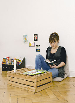 Eine Frau liest in einem Buch und sitzt dabei am Boden hinter einer alten Apfelsinenkiste als Tisch