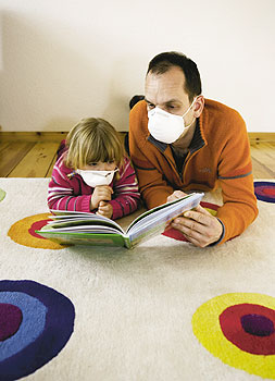 Mann liest einem Kind mit Gesichtsmasken auf gesundheitsschädlichem Teppich aus einem Buch vor