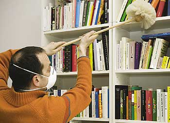 Mann mit Gesichtsmaske wischt Staub in einem Bücherregal