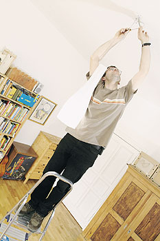 Mann beim Ersetzen einer Deckenlampe, auf einer zu kurzen und kippeligen Leiter