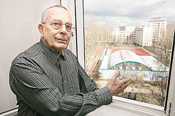 Günther Kunath schaut am Fenster, hinter ihm die neu gestaltete Turnhalle gegenüber seiner Wohnung