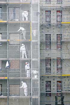 Bauarbeiter auf einem mit einem Netz gesicherten Gerüst bei Sanierungsarbeiten an einer Fassade