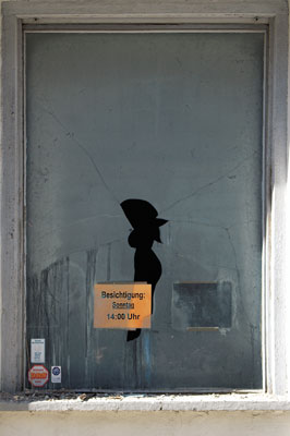 Zugenageltes Fenster mit zerbrochener Scheibe, dahinter ein Schild mit Aufschrift: 'Besichtigung Sonntag 14.00 Uhr'