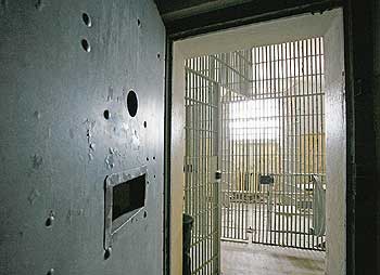Blick durch eine Gefängnistür in einen vergitterten Raum