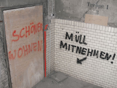 Provisorische Eingangstür mit der Aufschrift 'Schöner Wohnen', neben dem Eingang weist eine auf die Wand aufgesprühte Inschrift darauf hin: 'Müll mitnehmen'