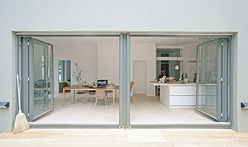 Zwei große, breite, geöffnete Glastüren führen in ein geräumiges Zimmer