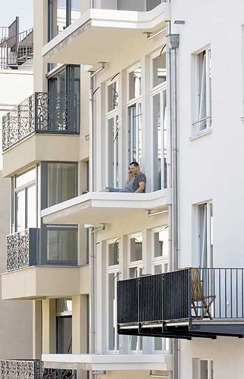 Fassade mit Balkonen, auf einem Balkon ohne Geländer sitzt ein Mann
