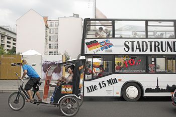 Rikscha-Fahrer mit Touristen und Stadtrundfahrten-Bus