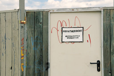 Stahltür in einem Holzlattenzaun mit der Aufschrift 'Privataussicht - Betrachten verboten'