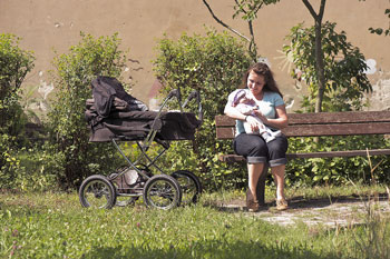 Frau mit Baby im Arm und Kinderwagen auf einer Parkbank