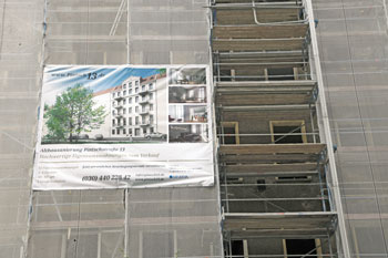 Werbeplakat für Eigentumswohnungen an eingerüstetem Mietshaus