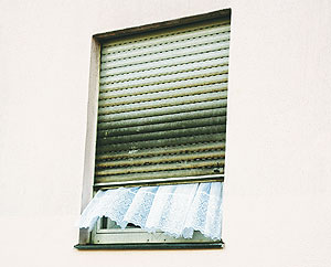 Fenster mit halb heruntergelassener Jalousie, unter der eine wehende Gardine hervorschaut