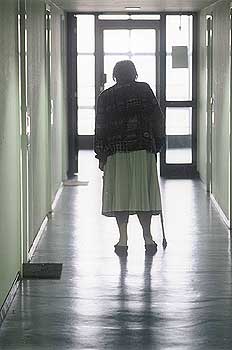 Alte Frau mit Gehhilfe nähert sich einer lichthellen Ausgangstür