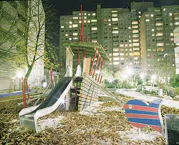 Beleuchteter Kinderspielplatz bei Nacht vor Hochhauskulisse