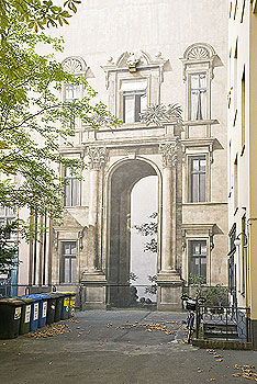 Fassadenmalerei simuliert Architektur: Stuckverziertes Eingangsportal und Fenster auf einer kahlen Wand