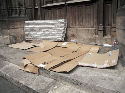 Matratze und auf dem Boden liegende Pappkartons auf den unüberdachten Eingangsstufen eine Gebäudes