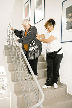 Betreuerin hilft einer Betreuten beim Treppensteigen