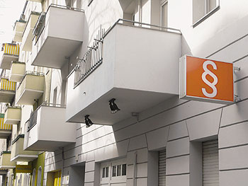 Ein oranges Firmenschild mit einem Paragraf-Zeichen an einer frisch sanierten Hausfassade