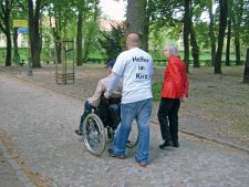 Helfer im Kiez, der einen Mann im Rollstuhl schiebt