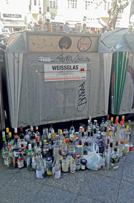 Leere Flaschen stehen vor und auf einem Weissglas-Container