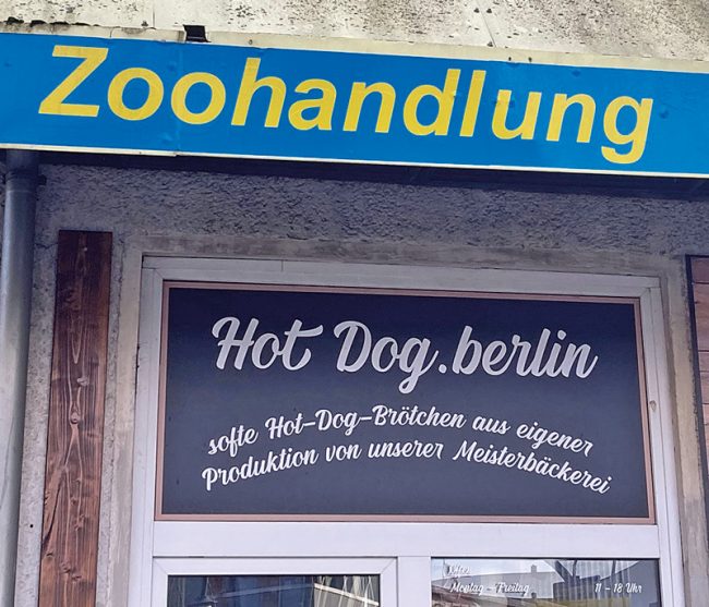 Schild mit Aufschrift "Zoohandlung" über einem Fenster mit dem Schriftzug "Hot Dog Berlin" Bäckerei