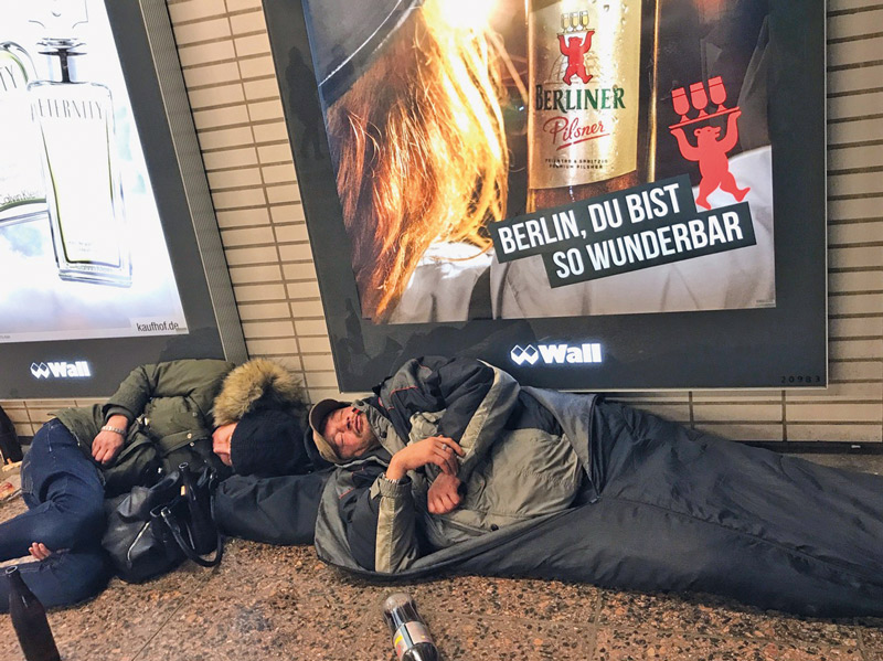 Schlafende Obdachlose vor einem Wall-Plakat