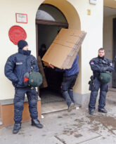 Arbeiter tragen unter Polizeischutz Umzugskartons ins Haus