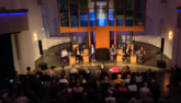 Das Foto zeigt aus der Schrägperspektive von oben das Altarinsel der Genezarethkirche in Berlin Neukölln. Vier Spitzenkandidat:innen von CDU, SPD, Grüne und Linke sitzen auf dem Podium. Im Vordergrund ist das Publikum zu sehen.